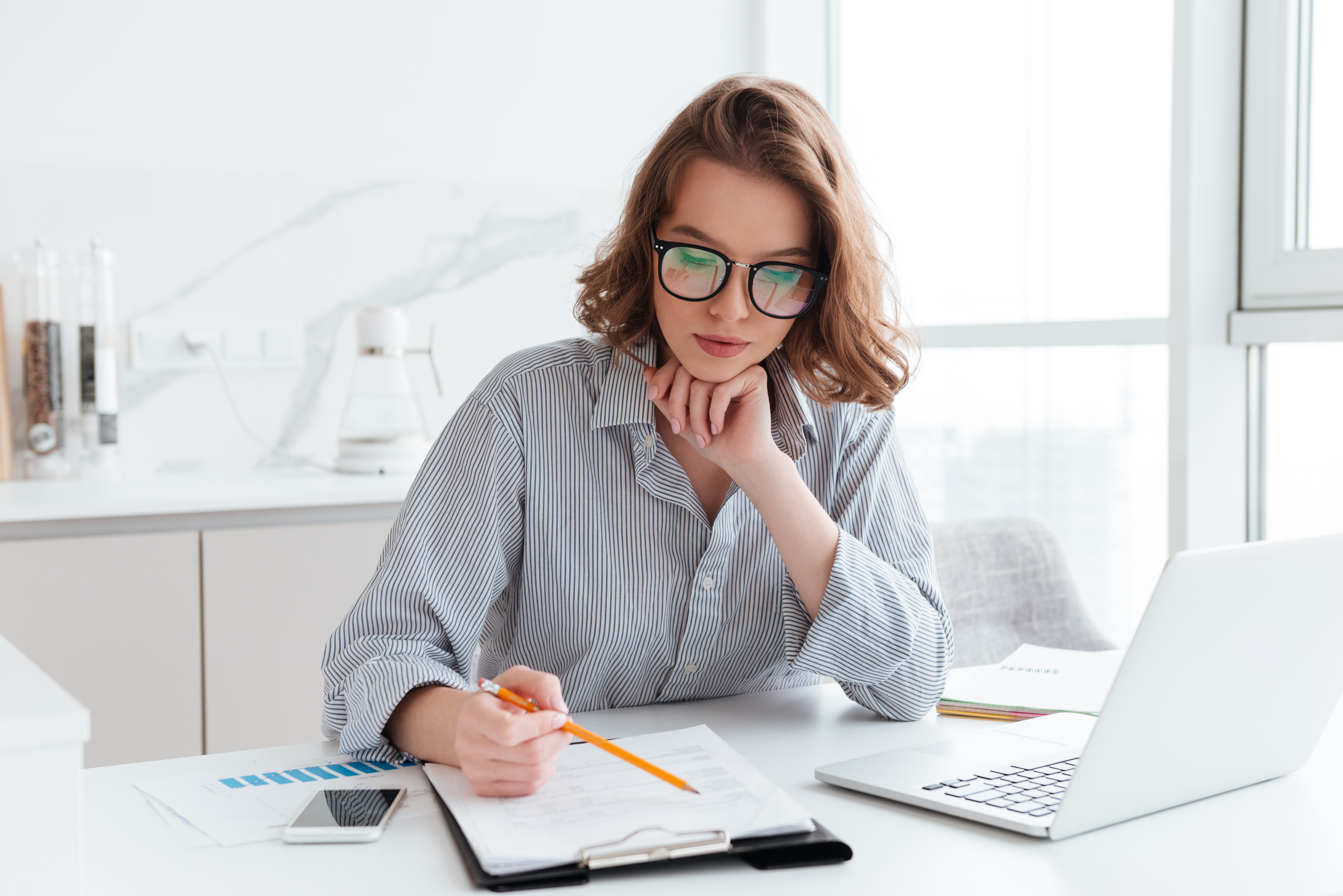 young concentrated businesswoman in glasses and striped shirt working with papers at home ¿Cómo manejar las finanzas un emprendimiento?